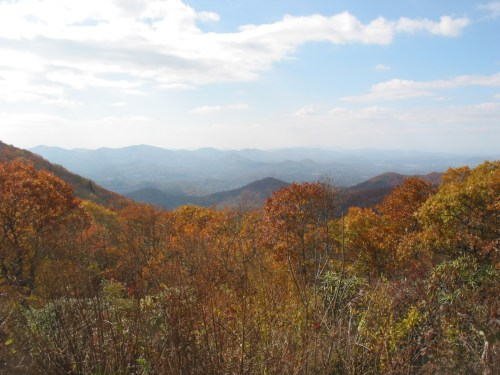 A scenic view of rolling mountains covered in autumn foliage under a partly cloudy sky.