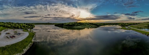 A serene lake at sunset, reflecting clouds and trees, with a small beach area and a winding path along the shore.