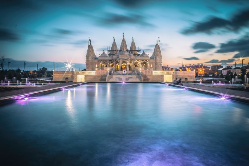 A stunning temple illuminated at dusk, reflecting in a serene water pool with colorful lights.