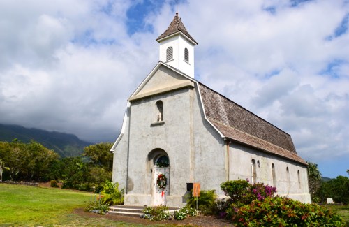 A quaint church with a steeple, surrounded by greenery and colorful flowers, under a partly cloudy sky.