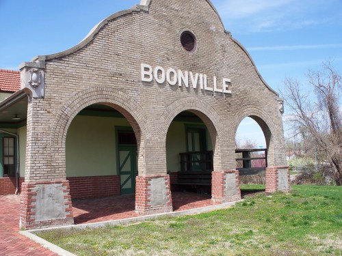 Historic Boonville train station with arched entrance and brick facade, surrounded by green grass and trees.