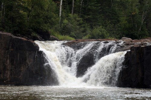A serene waterfall cascading over rocky cliffs, surrounded by lush green trees and a calm river below.