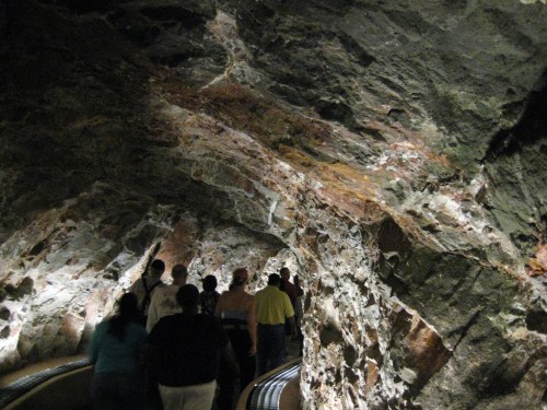 A group of people walking through a dimly lit rock tunnel with textured stone walls.