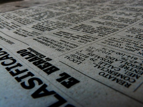 Close-up of a newspaper page with various articles and listings, slightly tilted for a dynamic perspective.