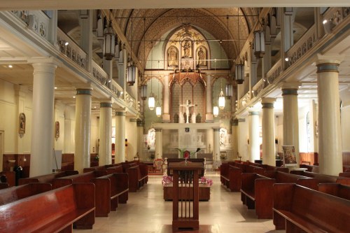 Interior of a church featuring wooden pews, tall columns, and an ornate altar with religious artwork.