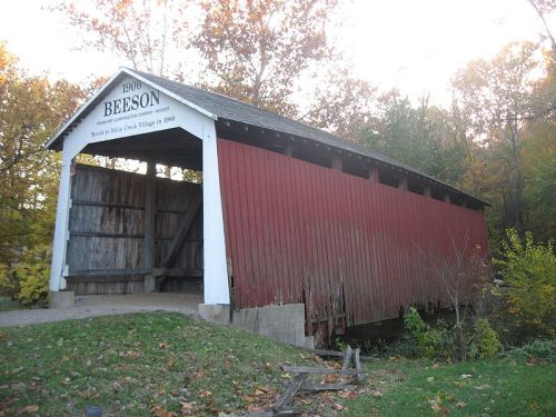 A red covered bridge with a white sign reading "Beeson 1900," surrounded by trees in autumn foliage.