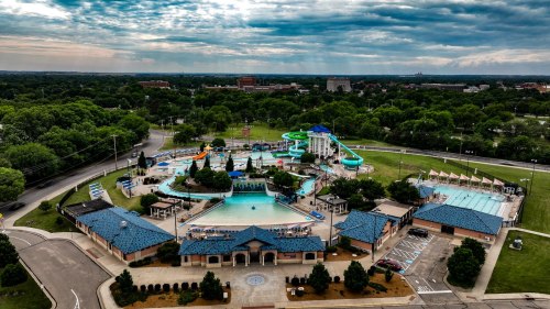 Aerial view of a water park featuring pools, slides, and green landscaping under a cloudy sky.