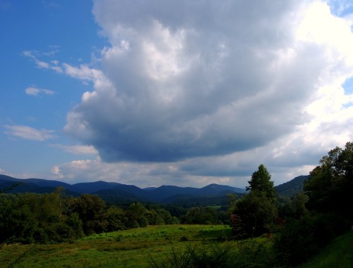 A scenic view of rolling mountains under a cloudy sky, with lush green fields in the foreground.