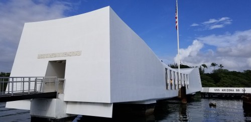 The USS Arizona Memorial, a white, modern structure over water, with a flagpole and blue sky in the background.