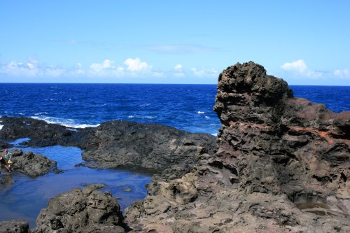Rocky coastline with a clear blue ocean and sky, featuring a person exploring the tide pools.