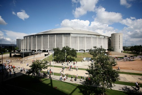 A large, modern arena surrounded by people walking on a sunny day with clouds in the sky.