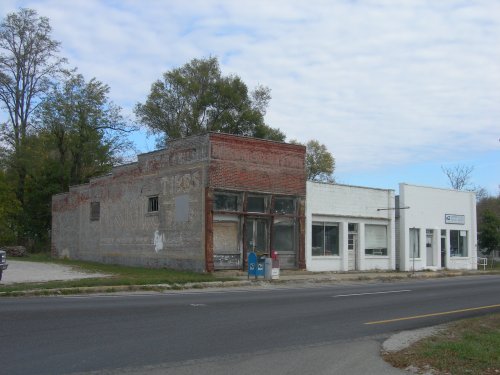 Abandoned brick building next to a white structure, both showing signs of wear, set against a cloudy sky.