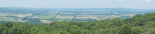 A panoramic view of lush green fields and rolling hills under a clear blue sky.