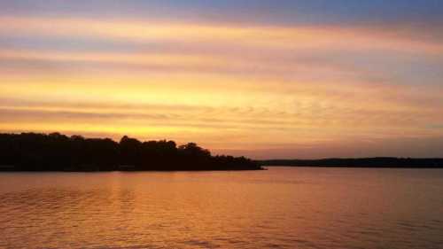 A serene sunset over a calm lake, with colorful clouds reflecting on the water's surface.