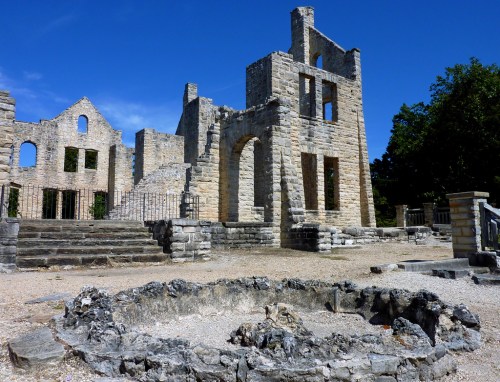 Ruins of a stone building under a clear blue sky, with remnants of walls and a circular stone foundation in the foreground.