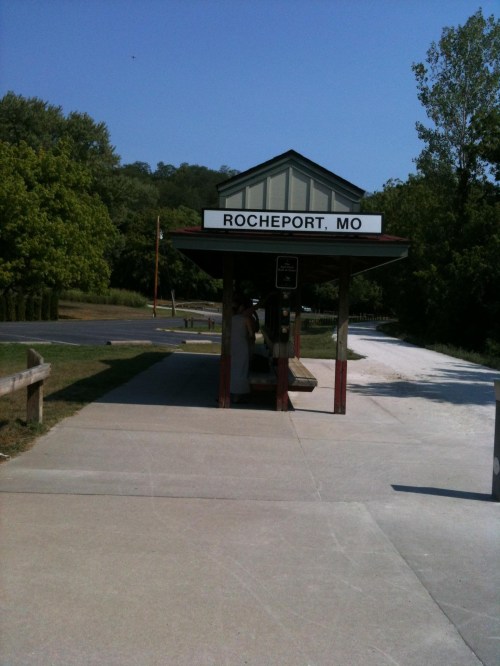 A small train station in Rocheport, MO, surrounded by trees and a clear blue sky.