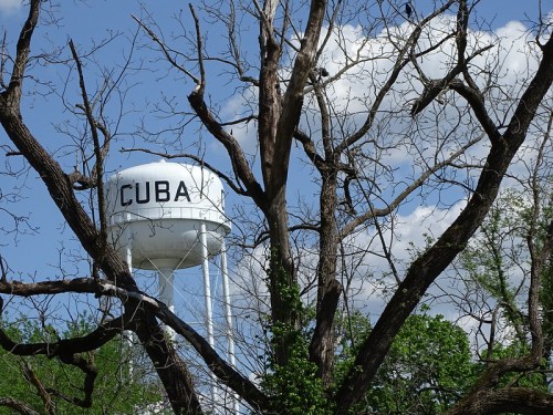 A water tower labeled "CUBA" stands behind a leafless tree against a blue sky with clouds.