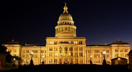 The illuminated facade of a grand capitol building at night, showcasing its dome and architectural details.