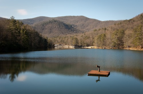 A serene lake surrounded by mountains, with a small dock in the foreground and trees lining the shore.