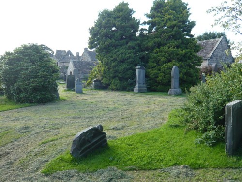 A peaceful cemetery scene with gravestones, lush greenery, and trees under a clear sky.