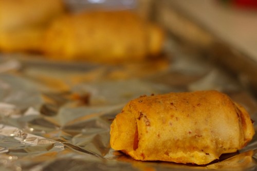A close-up of a golden-brown, baked snack roll on a sheet of aluminum foil.