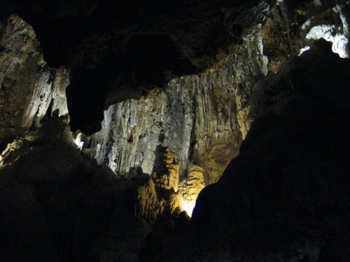 A dark cave interior with illuminated rock formations and stalactites, creating a dramatic and mysterious atmosphere.