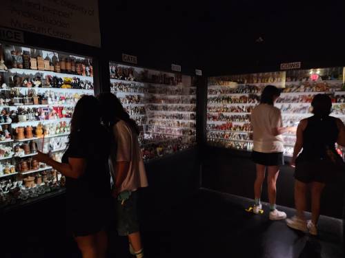 Visitors explore display cases filled with various figurines in a dimly lit museum exhibit.