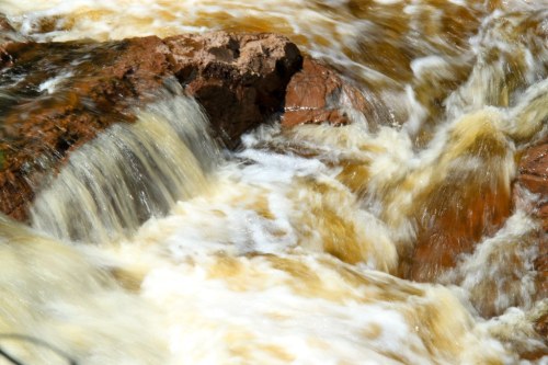 Rushing water flows over rocks, creating a dynamic and textured scene of nature's movement.
