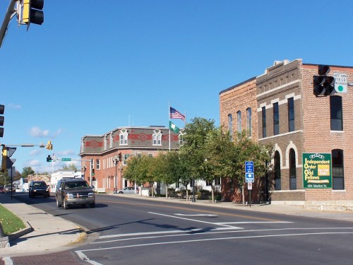 A street view featuring brick buildings, traffic lights, and an American flag, with clear blue skies above.