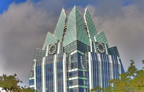 A modern skyscraper with a distinctive angular roof and glass facade, set against a cloudy sky.