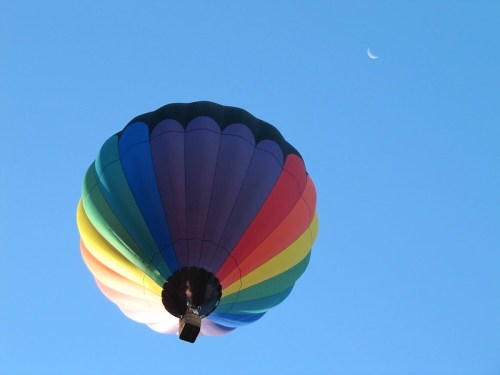 A colorful hot air balloon floats against a clear blue sky with a crescent moon visible in the background.