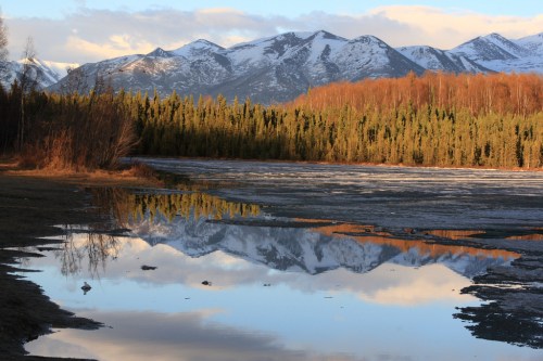 A serene landscape featuring snow-capped mountains, a forest, and a calm lake reflecting the scenery.