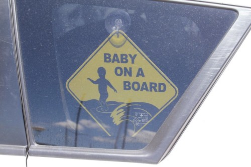 A yellow diamond-shaped sign on a car window reads "Baby on a Board," featuring a silhouette of a child.
