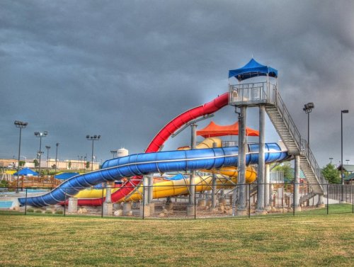 Colorful water slides with a tall tower, surrounded by a grassy area and cloudy skies in the background.