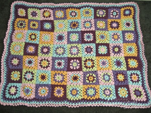 A colorful crocheted blanket featuring a grid of floral squares in pastel shades and dark purple.