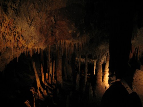 A dimly lit cave interior featuring stalactites and stalagmites, creating a mysterious underground landscape.