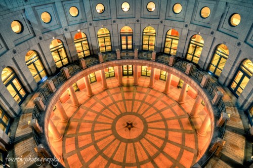 Aerial view of a circular atrium with arched windows and illuminated columns, showcasing intricate floor patterns.