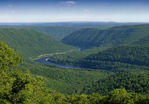 A panoramic view of lush green mountains and a winding river in a valley under a clear blue sky.