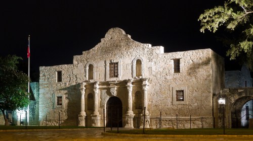 The Alamo illuminated at night, showcasing its historic stone architecture and surrounding trees.