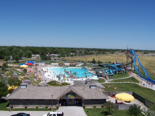 Aerial view of a water park with a large pool, water slides, and many people enjoying the sunny day.