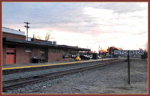 A train station in Hutchinson at sunset, featuring a sign and a yellow vehicle parked nearby.