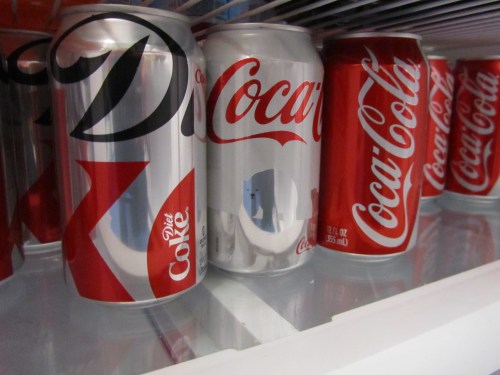 Cans of Diet Coke and Coca-Cola lined up in a refrigerator.