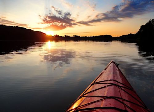 A red kayak on calm water at sunset, with colorful clouds reflecting on the surface.