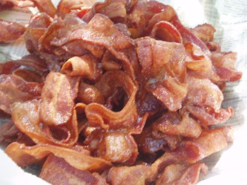 A close-up of crispy, golden-brown bacon strips piled together on a paper-lined surface.