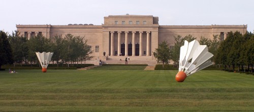 A large museum building with two oversized shuttlecock sculptures in the foreground, set on a grassy lawn.