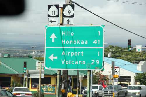 Green road sign indicating directions to Hilo (1 mile), Honokaa (41 miles), Airport (1 mile), and Volcano (29 miles).