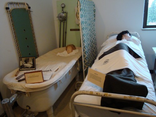 A vintage medical display featuring a bathtub and a hospital bed with a mannequin, showcasing historical healthcare practices.