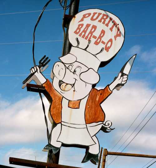 A cartoon pig chef holding a fork and knife, with a sign reading "Purity Bar-B-Q" above it.