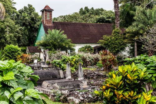 A serene cemetery with gravestones surrounded by lush greenery and a quaint church in the background.