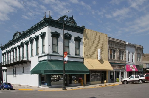 Historic buildings with ornate architecture, featuring a white structure and a tan storefront, under a blue sky.